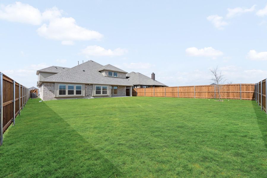 Large backyard with green lawn, wood privacy fence, and brick home with covered patio in background