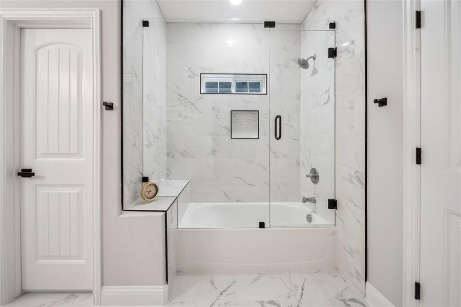 Bathroom featuring a bathtub with a clear glass enclosure and black hardware, white tile surround, and a recessed window