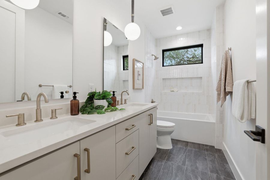 Contemporary bathroom featuring a double vanity with light-toned cabinetry, brushed nickel hardware, and an integrated white countertop with dual sinks