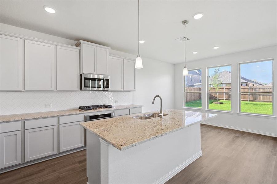 Kitchen with tasteful backsplash, a kitchen island with sink, wood-type flooring, sink, and pendant lighting