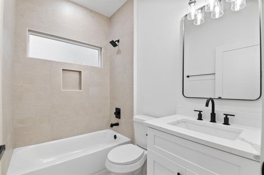 Modern bathroom with a sleek design featuring a bathtub with built-in niche, matte black fixtures, and a large vanity mirror. The space is bright with neutral tiles and a stylish light fixture.