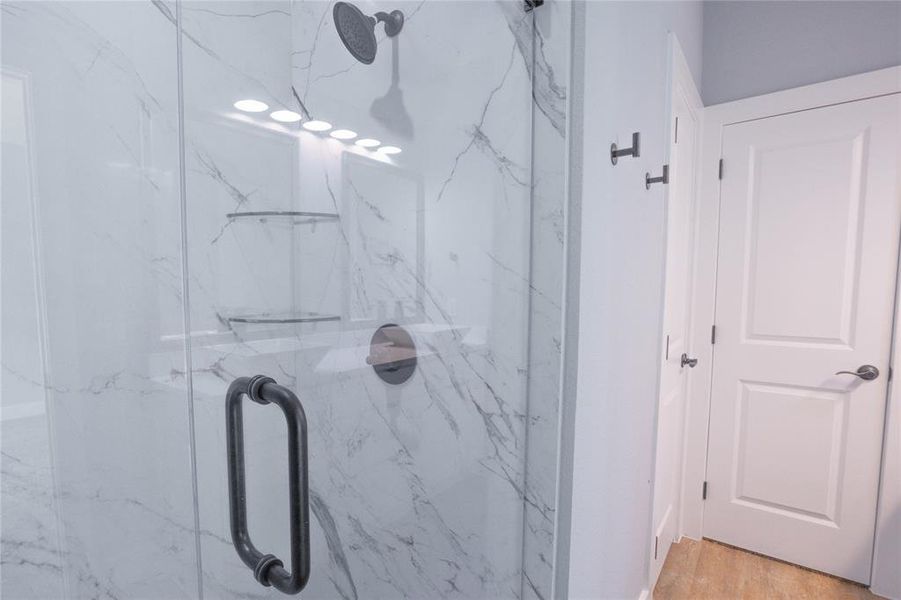 Bathroom with a marble finish shower and wood finished floors