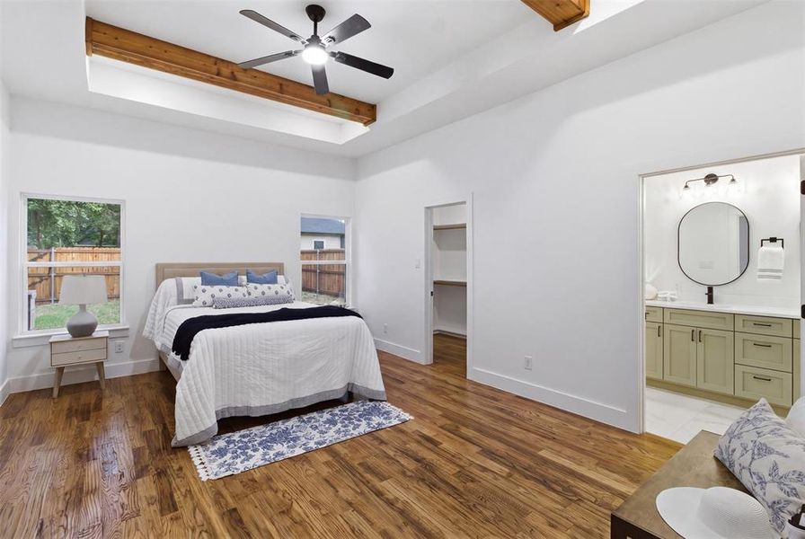 Spacious room featuring wood-finish flooring, a tray ceiling with exposed wood beams, and a ceiling fan