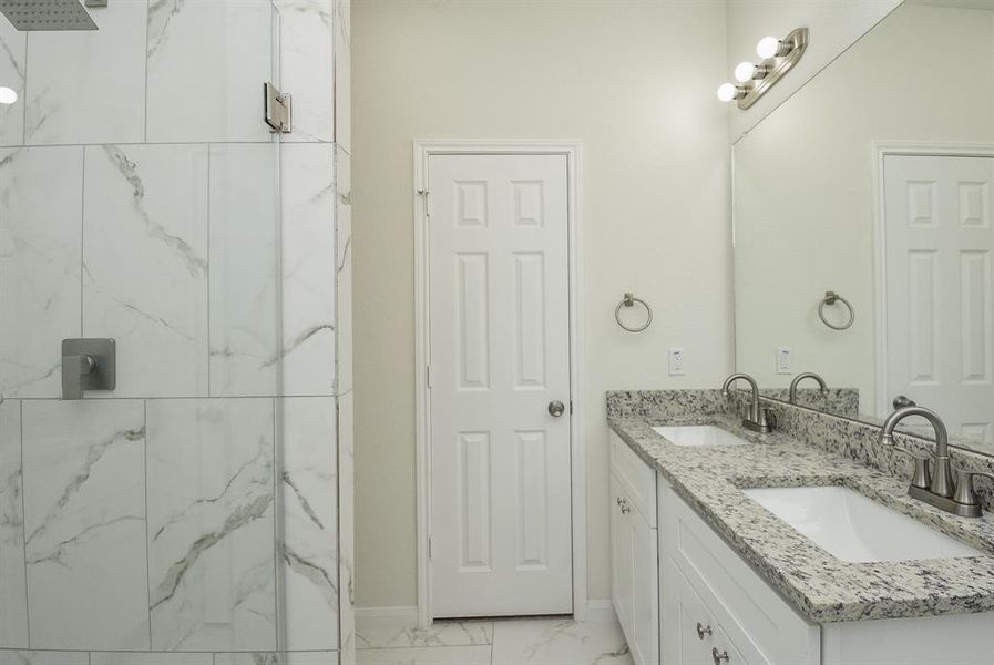 Modern bathroom interior with double sink vanity, marble tiles, white door, and wall-mounted light fixture.