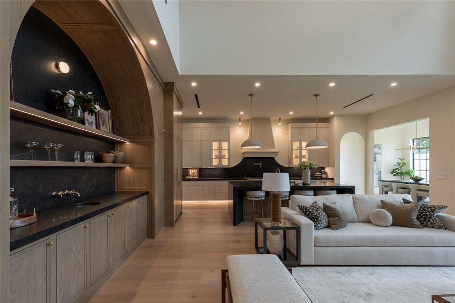 The wet bar is a true labor of craftsmanship, featuring a hand-carved stone arch built up the wall with millimeter precision and framed in warm paneling for added depth. A Native Trails sink, wall-mounted faucet, and integrated channel lighting give it a sculptural presence, while the rich black stone surface and custom shelving elevate it to an artful focal point in the heart of the home. The wet bar is a true labor of craftsmanship, featuring a hand-carved stone arch built up the wall with millimeter precision and framed in warm paneling for added depth. A Native Trails sink, wall-mounted faucet, and integrated channel lighting give it a sculptural presence, while the rich black stone surface and custom shelving elevate it to an artful focal point in the heart of the home.