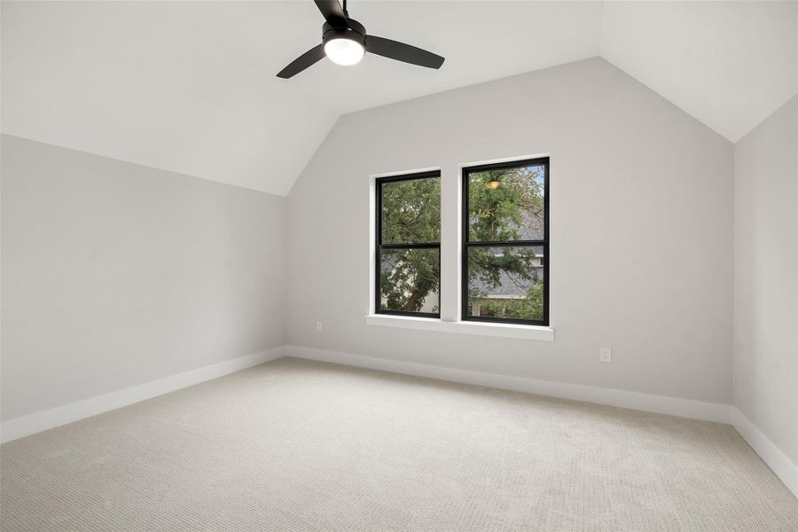 A well-lit bedroom featuring vaulted ceilings, a ceiling fan, and large windows overlooking lush greenery. A well-lit bedroom featuring vaulted ceilings, a ceiling fan, and large windows overlooking lush greenery.
