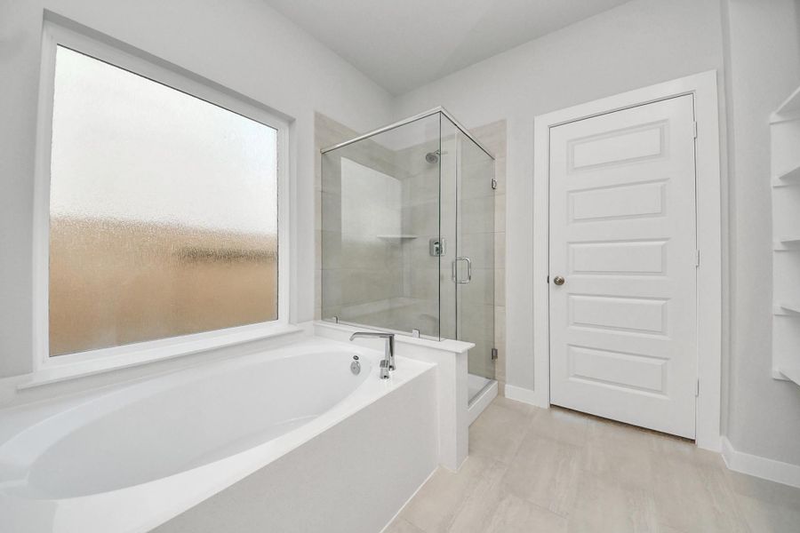 Indulge in a spa-like retreat within the confines of this primary bathroom. Delight in a spacious walk-in shower enveloped in stylish tile surround and unwind in a separate garden tub adorned with custom detailing. Sample photo of completed home with similar floor plan. Actual colors and selections may vary.