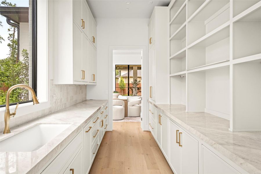 Elegant scullery with Taj Mahal countertops, floor-to-ceiling storage, sink, and dishwasher.