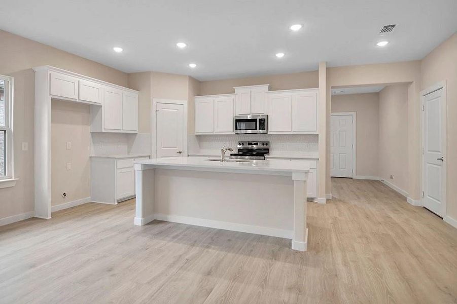 Kitchen with appliances with stainless steel finishes, light wood-style flooring, a center island with sink, light countertops, and tasteful backsplash Kitchen with appliances with stainless steel finishes, light wood-style flooring, a center island with sink, light countertops, and tasteful backsplash