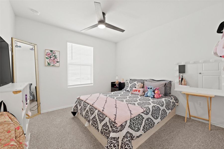 This spacious upstairs bedroom features plush carpeting, a modern ceiling fan, and a window that keeps the space feeling bright and airy.
