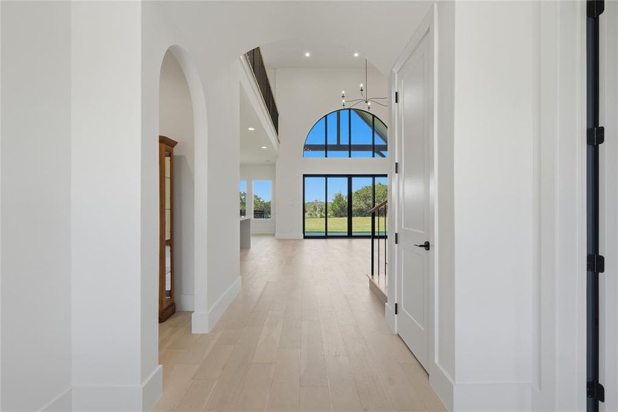 Bright entryway featuring light wood-finish flooring, an arched doorway, and white paneled doors with matte black hardware