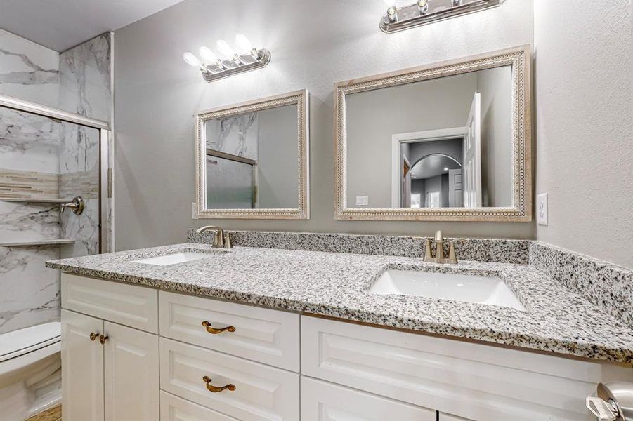 Bathroom with dual vanity, toilet, and a shower with shower door