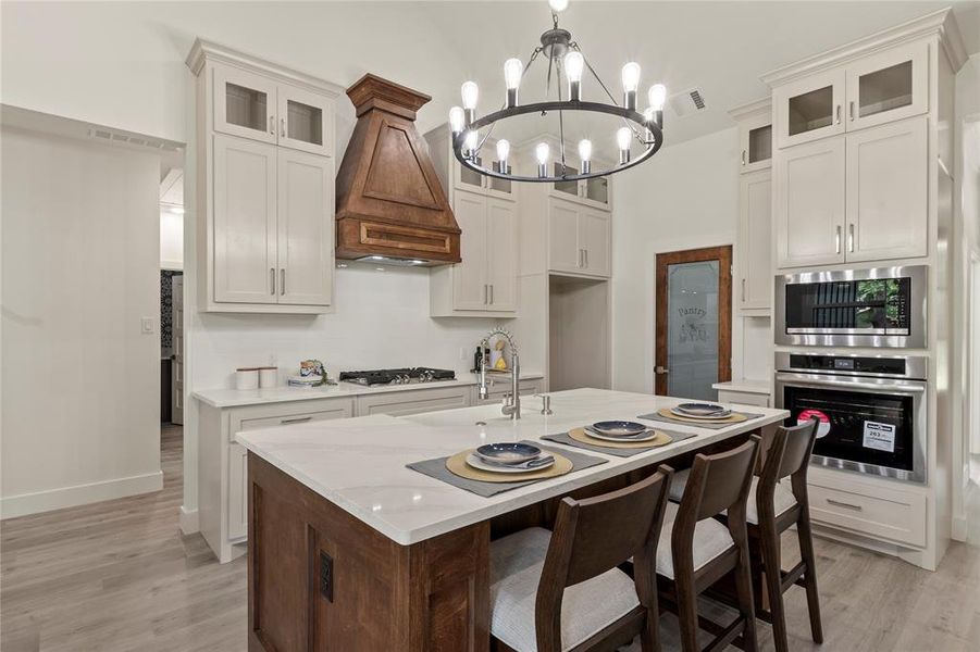 Kitchen featuring appliances with stainless steel finishes, a chandelier, a sink, premium range hood, and light wood-style floors