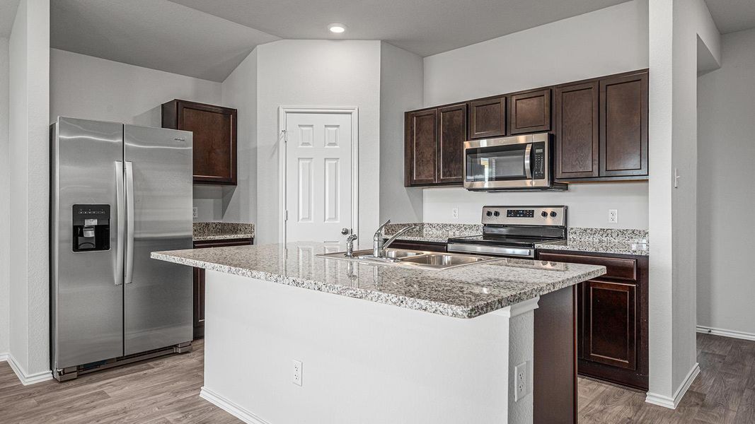 Kitchen with stainless steel appliances, dark wood finish cabinetry, light stone counters, a center island with sink, and light wood-style flooring Kitchen with stainless steel appliances, dark wood finish cabinetry, light stone counters, a center island with sink, and light wood-style flooring