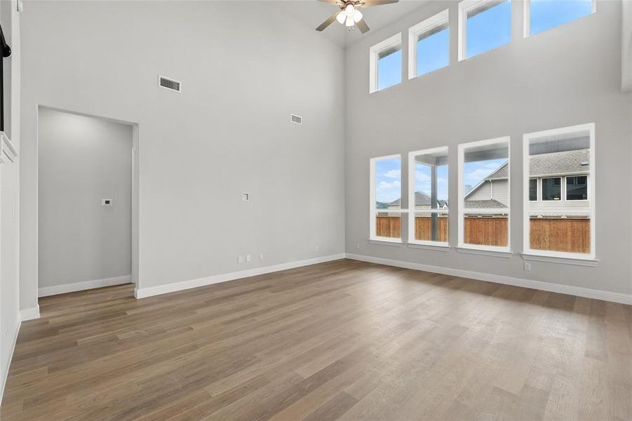 Unfurnished living room with a high ceiling, a ceiling fan, baseboards, and wood finished floors