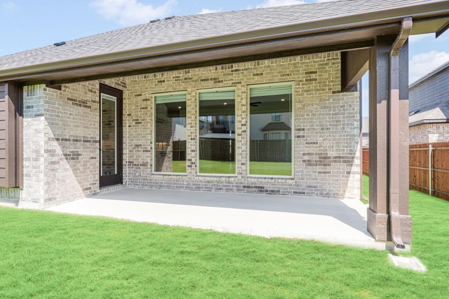 Covered back patio with concrete floor, brick exterior, large windows, and green lawn
