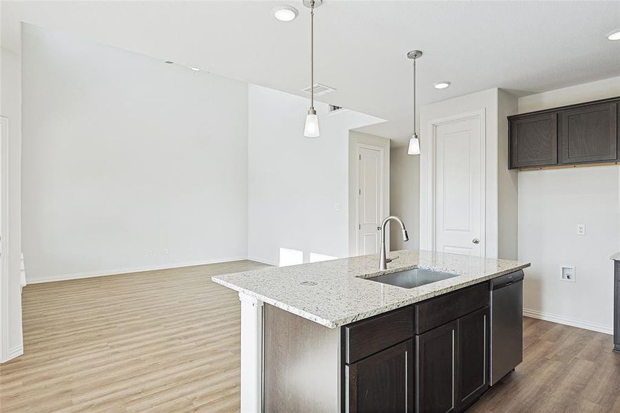 Kitchen with hanging light fixtures, a kitchen island with sink, light wood-type flooring, sink, and light stone counters