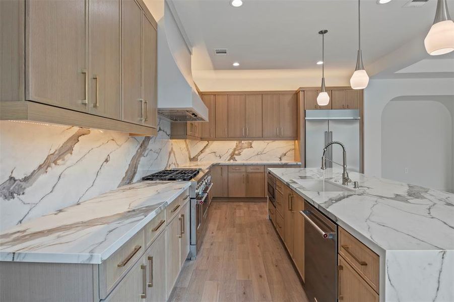 Kitchen with light stone counters, pendant lighting, light wood-type flooring, high quality appliances, and decorative backsplash Kitchen with light stone counters, pendant lighting, light wood-type flooring, high quality appliances, and decorative backsplash