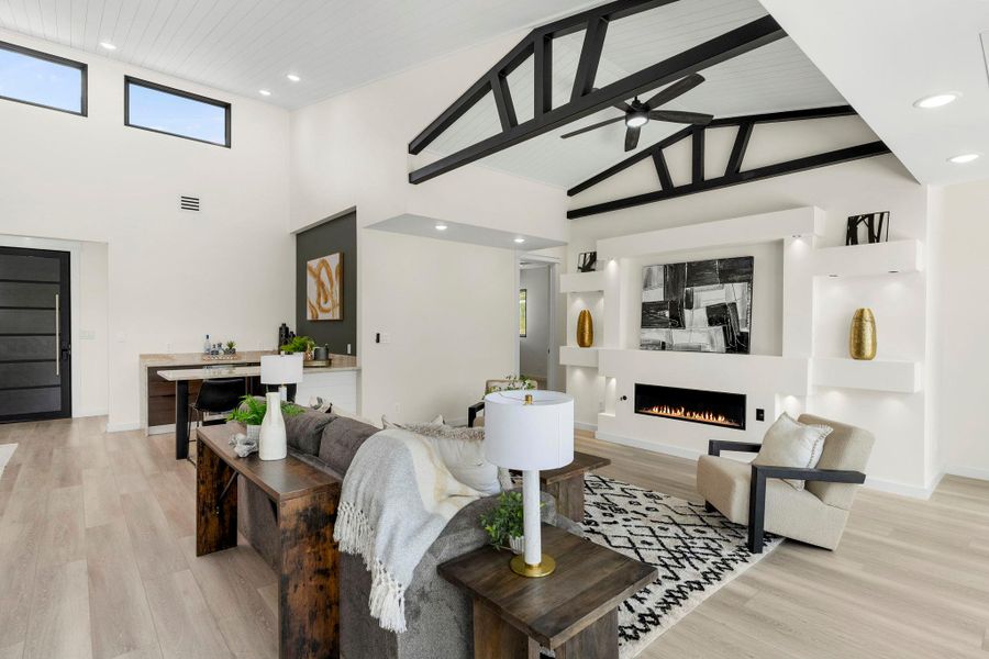 Living area featuring recessed lighting, light wood finished floors, a lit fireplace, a high ceiling, and a ceiling fan