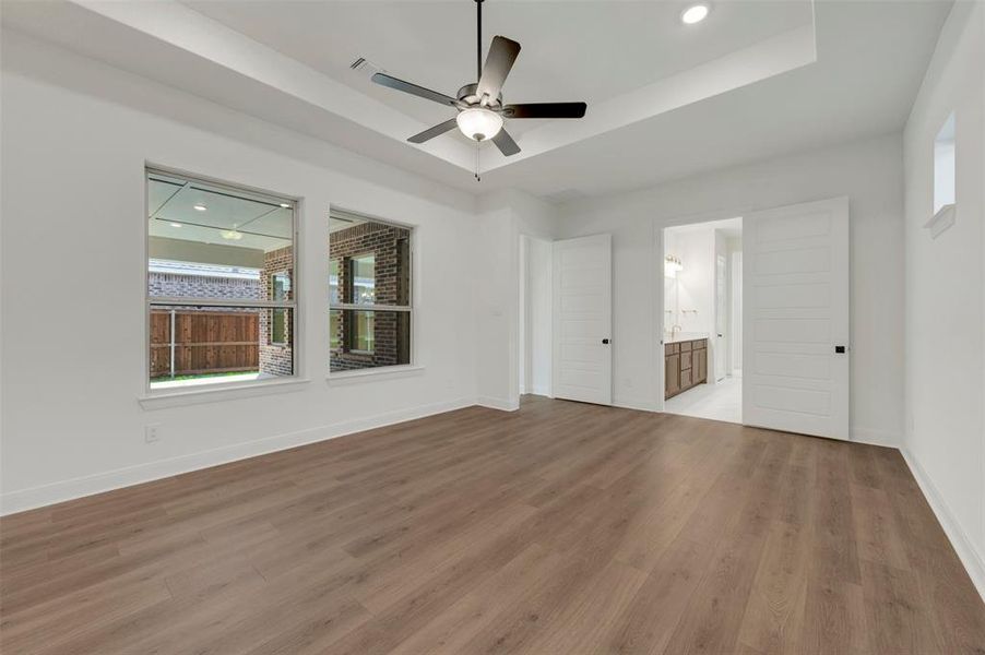 Spacious room featuring wood-finish flooring, a tray ceiling with a ceiling fan, and recessed lighting Spacious room featuring wood-finish flooring, a tray ceiling with a ceiling fan, and recessed lighting