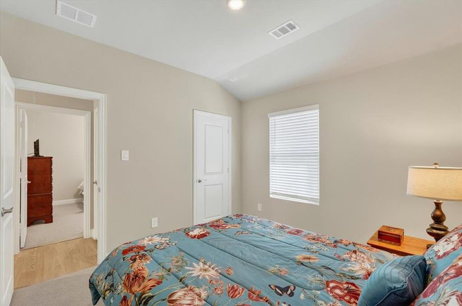 Bedroom with vaulted ceiling, light beige wall paint, single window with horizontal blinds, and a white two-panel interior door Bedroom with vaulted ceiling, light beige wall paint, single window with horizontal blinds, and a white two-panel interior door
