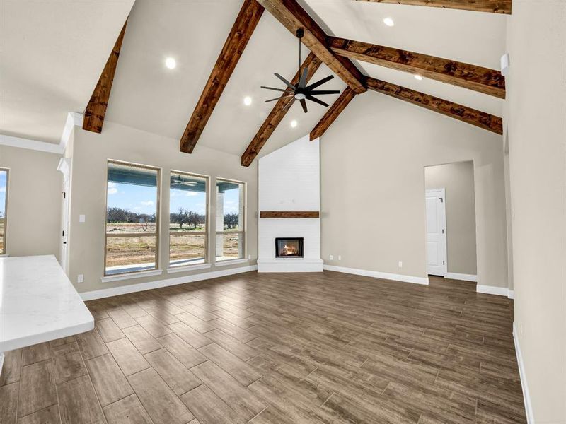 Unfurnished living room with a fireplace, high vaulted ceiling, beam ceiling, and ceiling fan