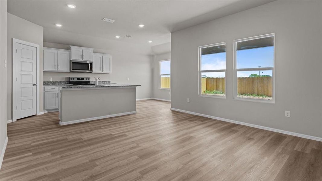 Kitchen featuring appliances with stainless steel finishes, open floor plan, light wood-style floors, a kitchen island with sink, and white cabinets Kitchen featuring appliances with stainless steel finishes, open floor plan, light wood-style floors, a kitchen island with sink, and white cabinets