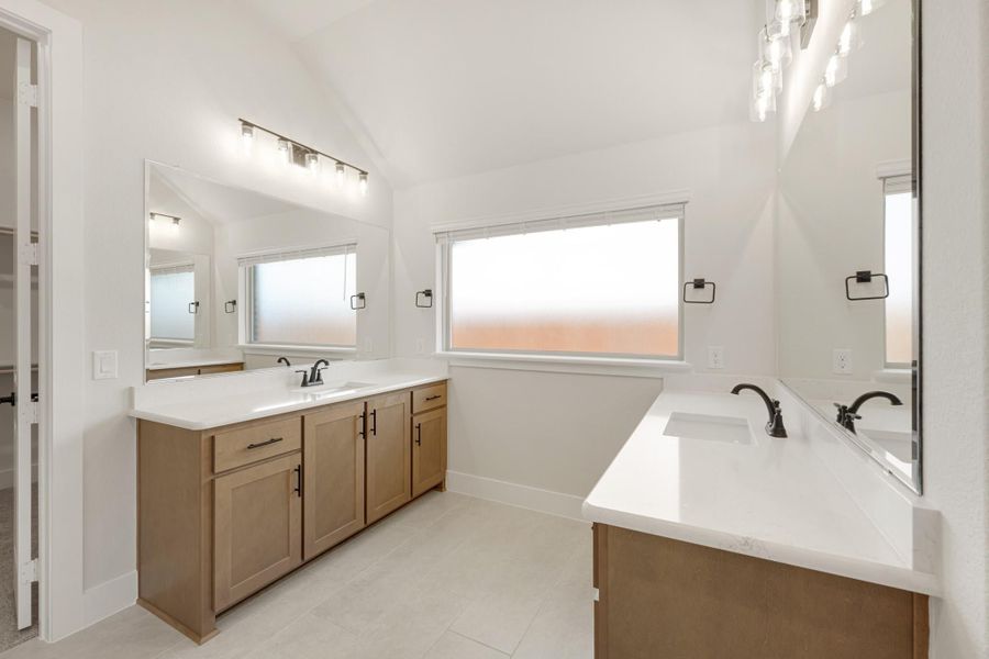 Bathroom with dual vanities, wood cabinets, white countertops, and vaulted ceiling with natural light
