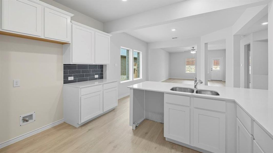 Kitchen featuring white cabinetry, tasteful backsplash, light wood-style flooring, a ceiling fan, and light stone counters Kitchen featuring white cabinetry, tasteful backsplash, light wood-style flooring, a ceiling fan, and light stone counters