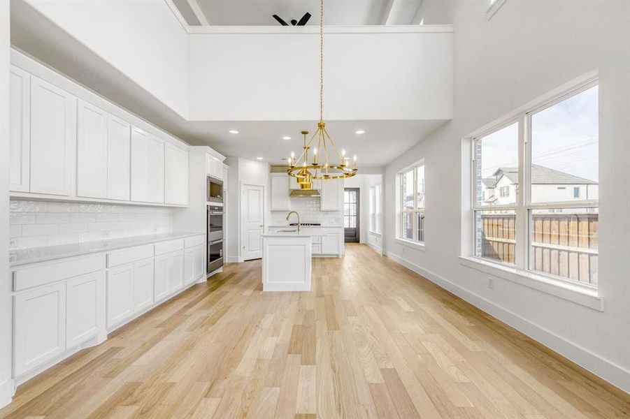 Kitchen with a chandelier, white cabinetry, light wood finished floors, decorative backsplash, and a center island with sink