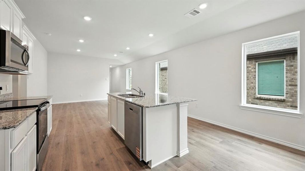 Open-concept kitchen and living area featuring wood-finish flooring, white cabinetry, recessed lighting, stainless steel appliances, and granite countertops Open-concept kitchen and living area featuring wood-finish flooring, white cabinetry, recessed lighting, stainless steel appliances, and granite countertops