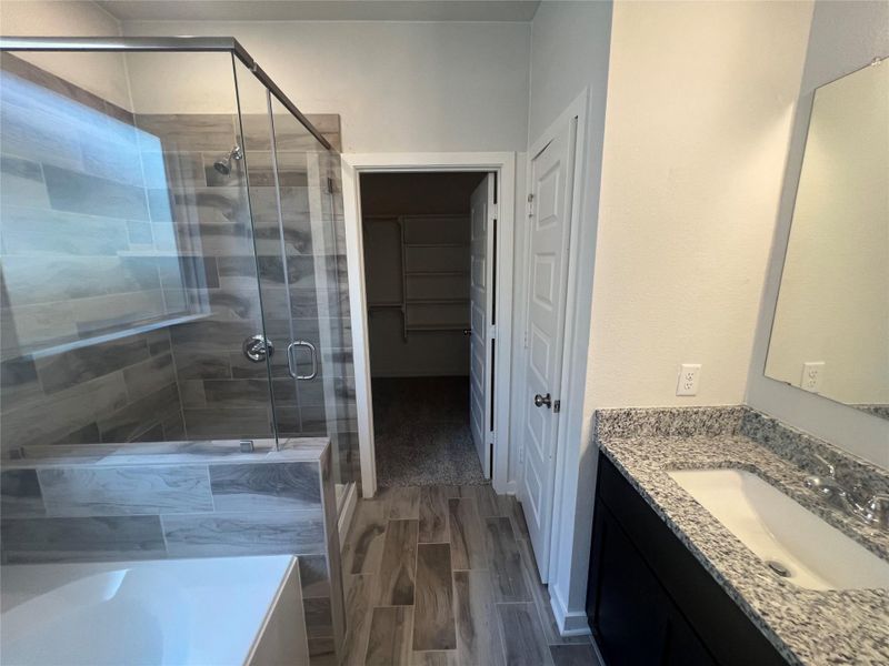 A well-appointed primary bathroom featuring a spacious shower and a vanity with stone counters.