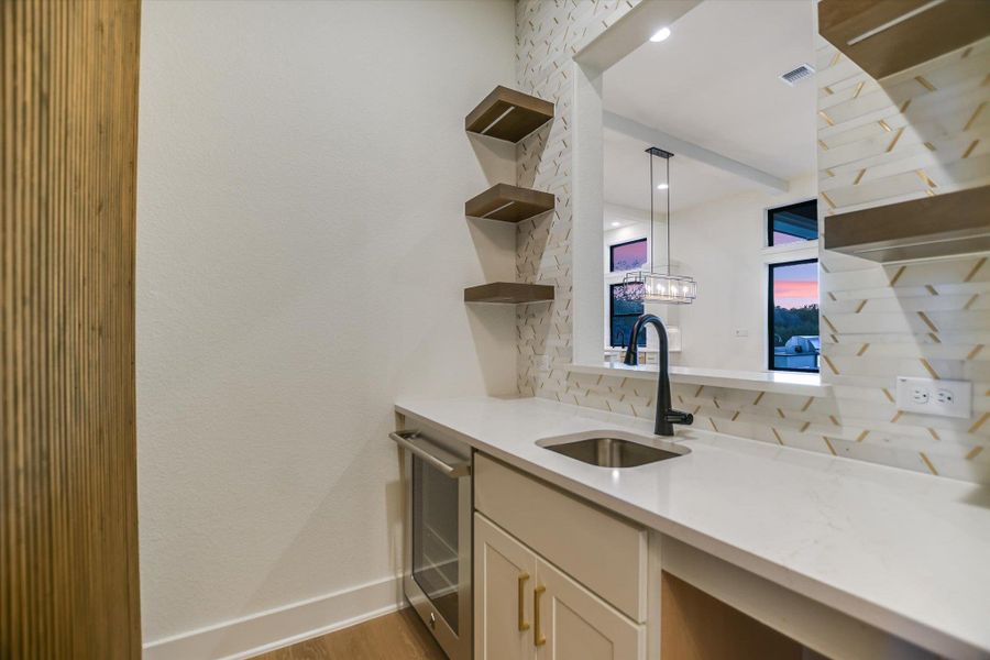Bar with open shelves, light stone countertops, pendant lighting, stainless steel dishwasher, and decorative backsplash