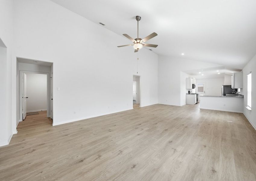Open-concept family room featuring a ceiling fan, wood-look vinyl flooring, and a sightline into the kitchen. Open-concept family room featuring a ceiling fan, wood-look vinyl flooring, and a sightline into the kitchen.
