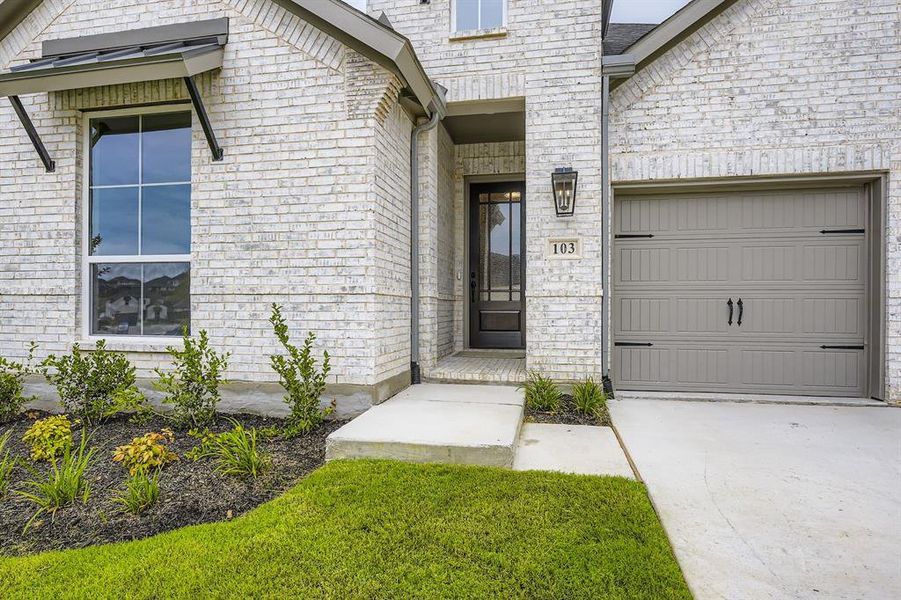 View of exterior entry featuring a garage, driveway, and brick siding