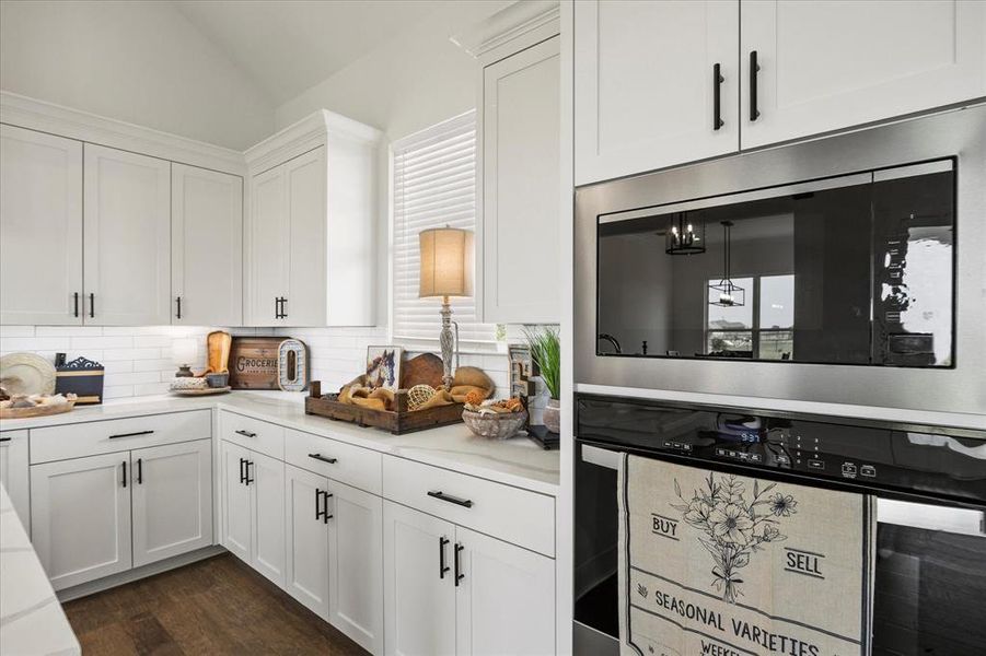 Kitchen with backsplash, stainless steel appliances, dark wood-type flooring, and white cabinetry