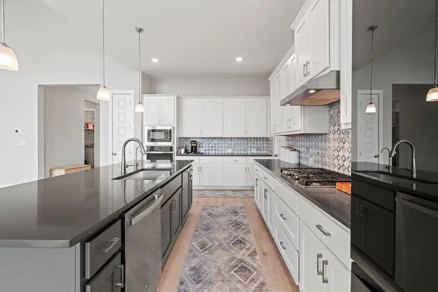 Kitchen with hanging light fixtures, white cabinetry, decorative backsplash, an island with sink, and stainless steel appliances Kitchen with hanging light fixtures, white cabinetry, decorative backsplash, an island with sink, and stainless steel appliances