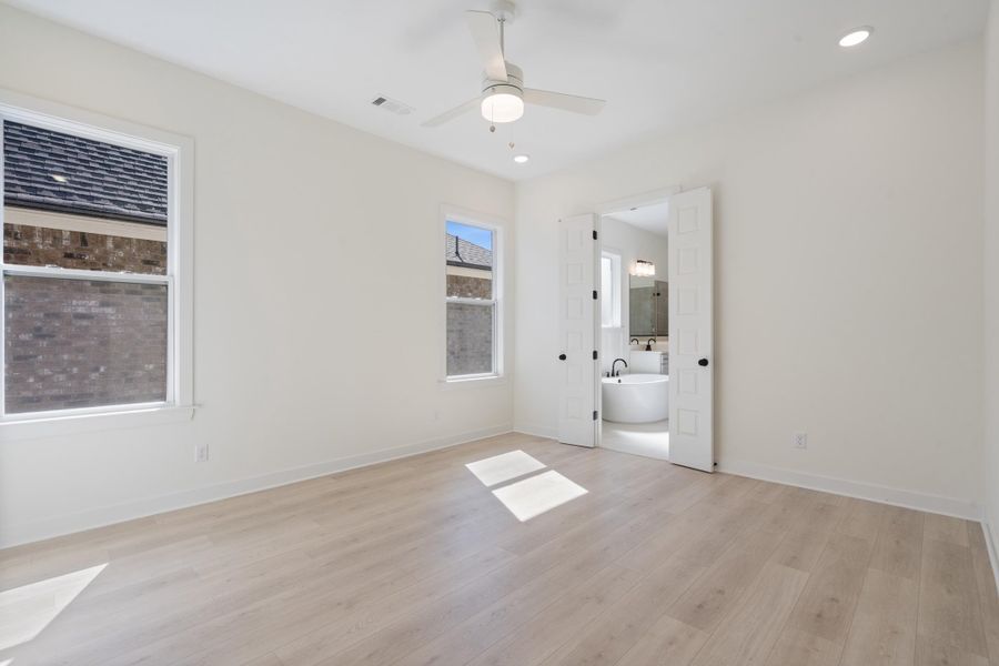 Neutral-toned wood-finish flooring, recessed lighting, white ceiling fan with integrated light fixture, and double-panel doors opening to a space with a freestanding soaking tub Neutral-toned wood-finish flooring, recessed lighting, white ceiling fan with integrated light fixture, and double-panel doors opening to a space with a freestanding soaking tub