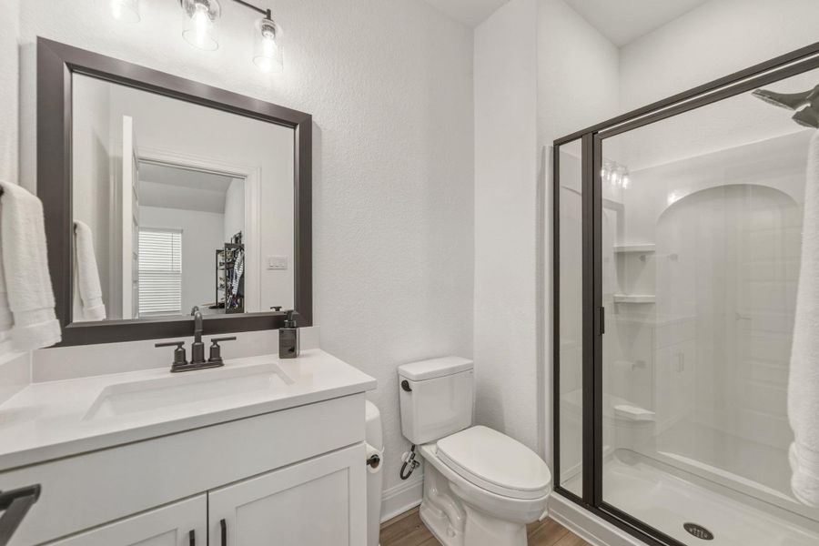 Ensuite bathroom featuring a white quartz vanity with an integrated sink, and a glass-enclosed shower with a curved back panel and built-in shelving