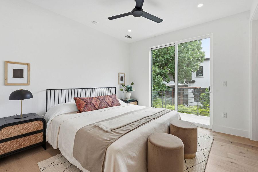 Light-filled room featuring wide-plank wood-finish flooring, a modern black ceiling fan, recessed lighting, white walls, and a sliding glass door opening to a private balcony with a metal railing