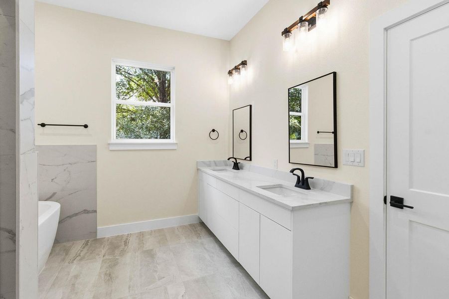 A well-lit primary bathroom featuring a double vanity, marble countertops, and a modern aesthetic. A well-lit primary bathroom featuring a double vanity, marble countertops, and a modern aesthetic.