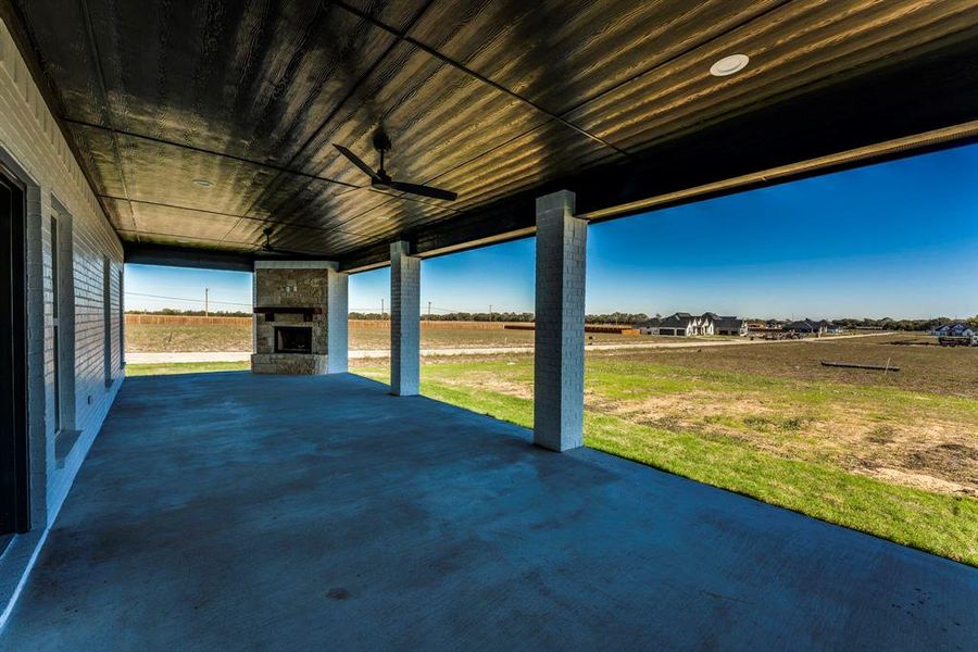 View of patio / terrace featuring an outdoor stone fireplace, ceiling fan, and a rural view