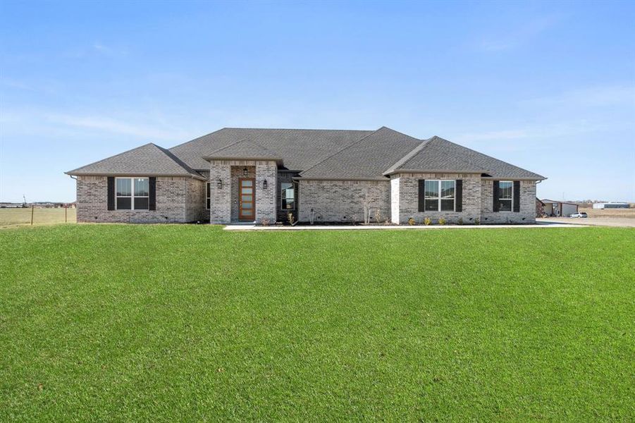 French country inspired facade featuring brick siding, roof with shingles, and a front yard