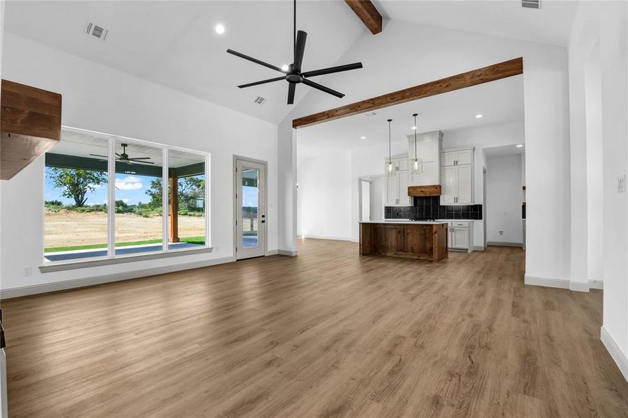 Unfurnished living room with ceiling fan, light hardwood / wood-style floors, beam ceiling, and high vaulted ceiling