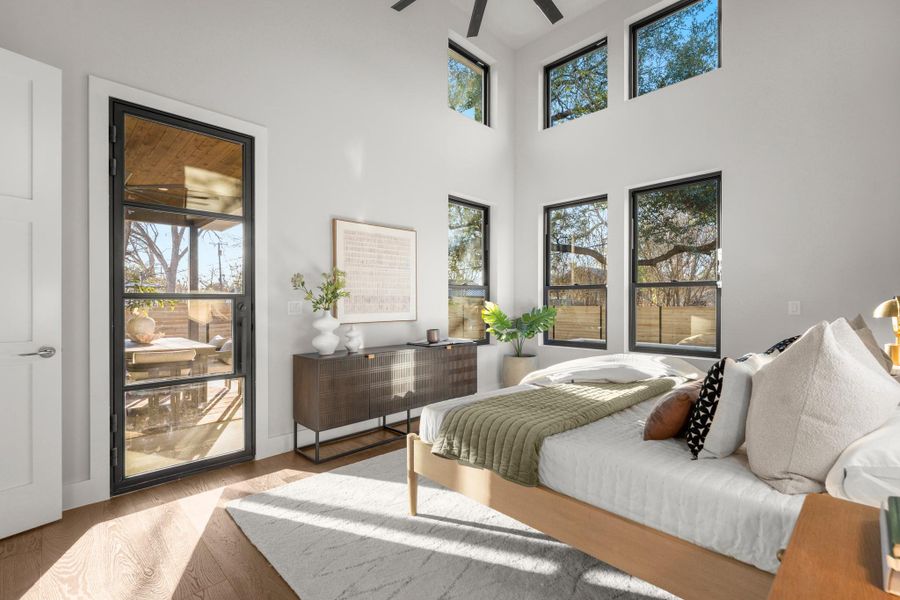 Bedroom with access to exterior, wood finished floors, multiple windows, and a high ceiling