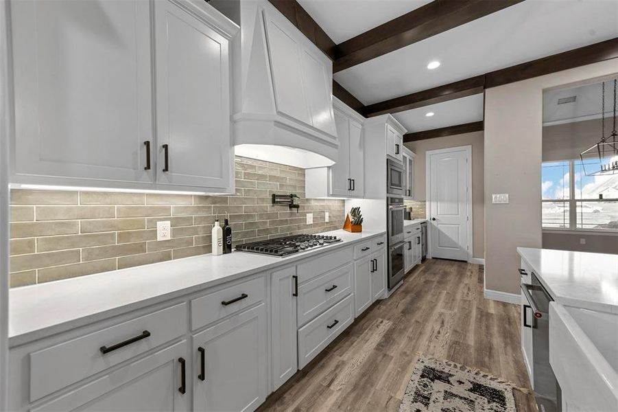 Kitchen featuring premium range hood, beam ceiling, appliances with stainless steel finishes, light hardwood / wood-style floors, and white cabinetry