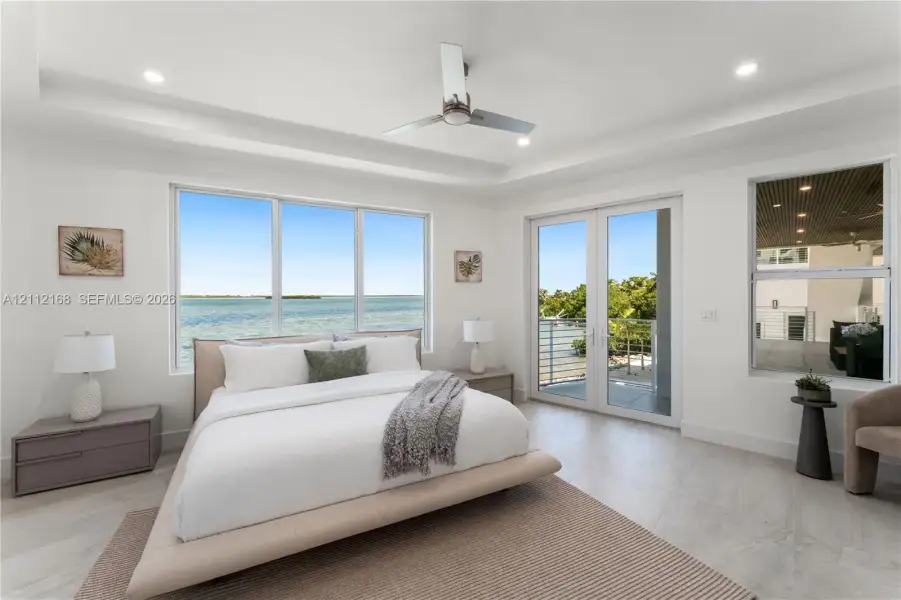 Tray ceiling with recessed lighting, floor-to-ceiling windows, modern ceiling fan, and glass-paneled double doors opening to a balcony Tray ceiling with recessed lighting, floor-to-ceiling windows, modern ceiling fan, and glass-paneled double doors opening to a balcony