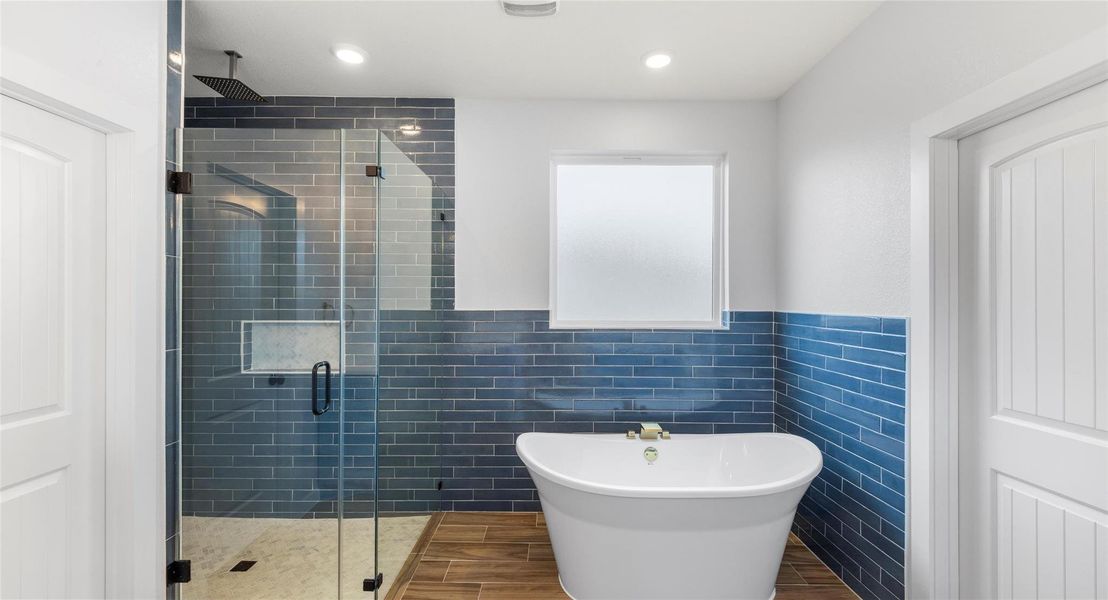 Bathroom featuring tile walls, a stall shower, wainscoting, a freestanding bath, and wood tiled floors