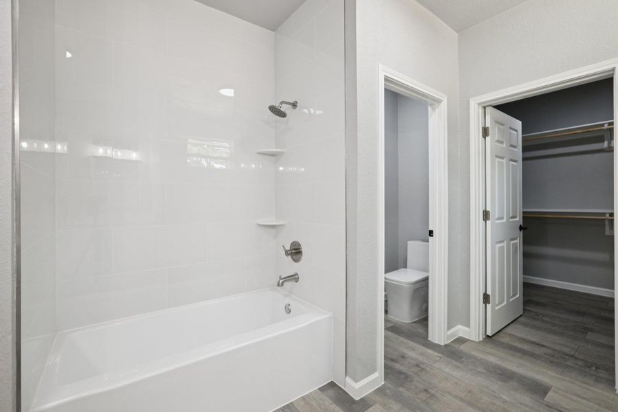 Bathroom featuring light wood-type laminate flooring shower / bathtub combination, and a spacious closet
