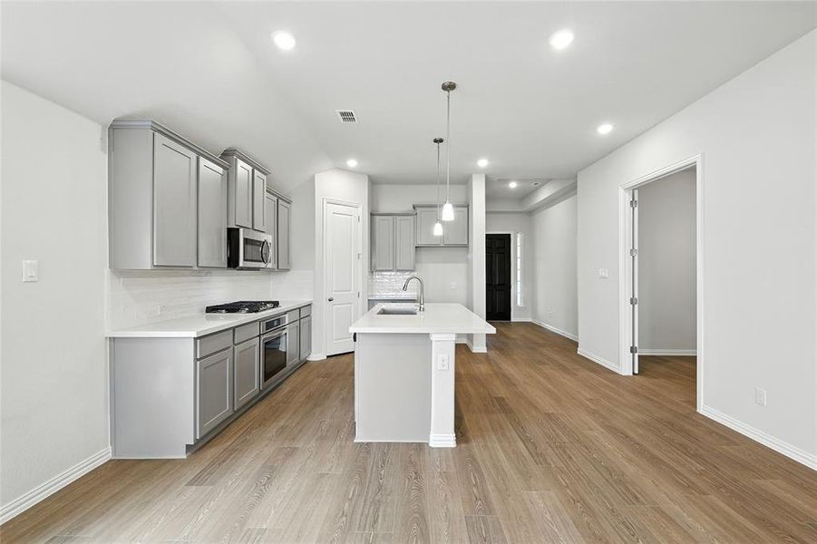 Kitchen with gray cabinetry, a center island with sink, light wood-style flooring, and pendant lighting
